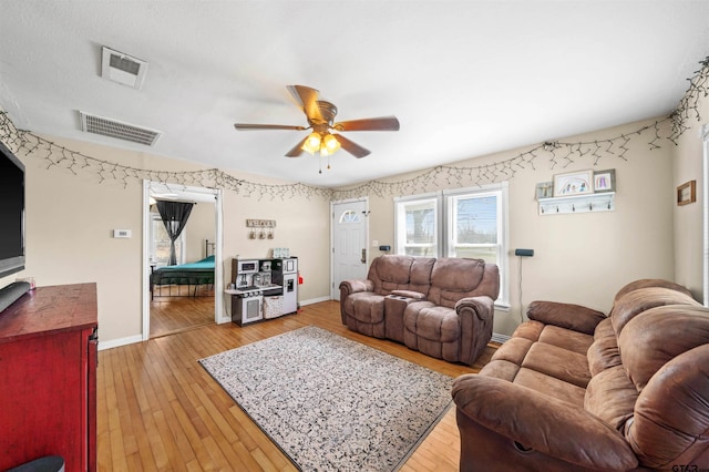 living room with light wood finished floors, visible vents, and baseboards