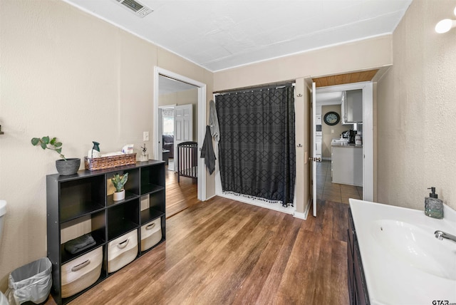 interior space featuring visible vents, a textured wall, a shower with shower curtain, wood finished floors, and vanity