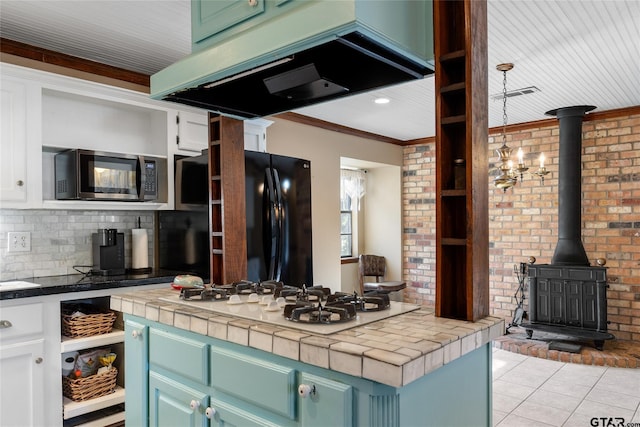 kitchen with tile countertops, range hood, white cabinetry, white gas cooktop, and a wood stove