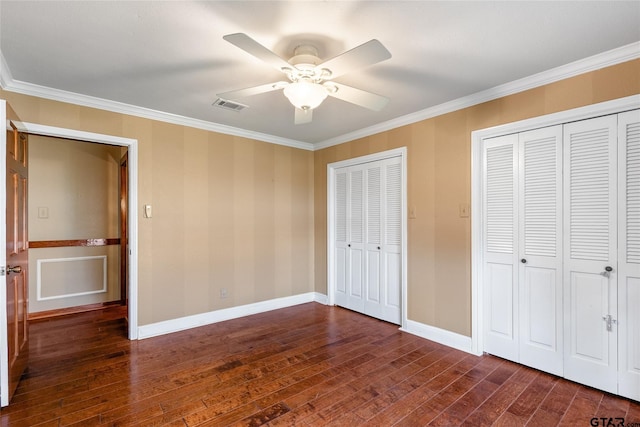 unfurnished bedroom with ceiling fan, crown molding, two closets, and dark hardwood / wood-style floors