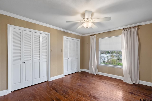 unfurnished bedroom with ceiling fan, dark wood-type flooring, ornamental molding, and two closets