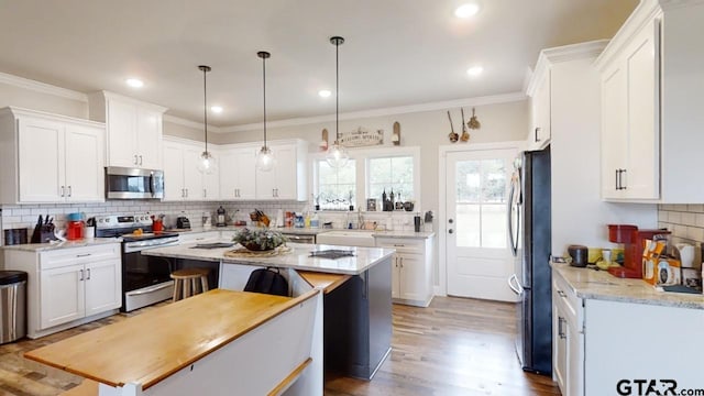 kitchen with ornamental molding, backsplash, wood finished floors, white cabinetry, and stainless steel appliances