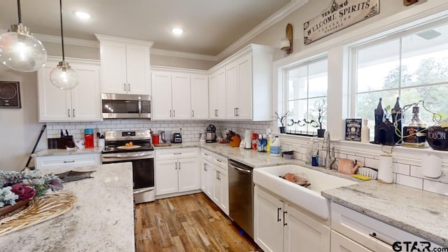 kitchen with a sink, stainless steel appliances, ornamental molding, and white cabinetry