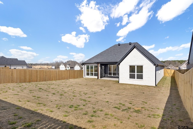 back of house featuring brick siding, roof with shingles, a fenced backyard, and a sunroom