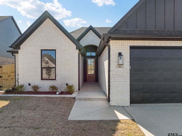 entrance to property featuring brick siding, board and batten siding, an attached garage, and fence