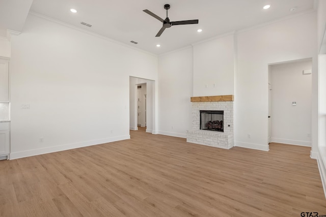 unfurnished living room with a fireplace, a towering ceiling, ornamental molding, ceiling fan, and light wood-type flooring