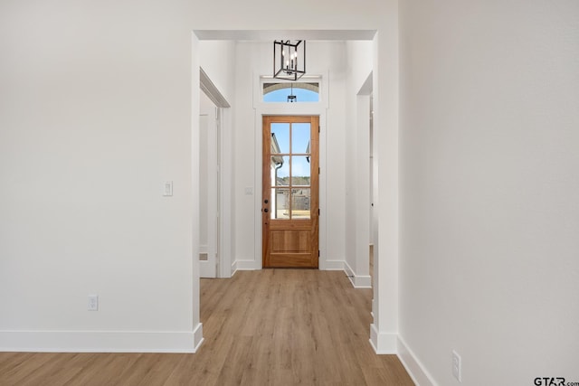 doorway to outside featuring light wood finished floors, an inviting chandelier, and baseboards