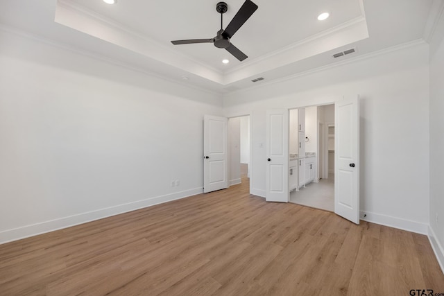 unfurnished bedroom featuring a tray ceiling, light wood-type flooring, visible vents, and crown molding