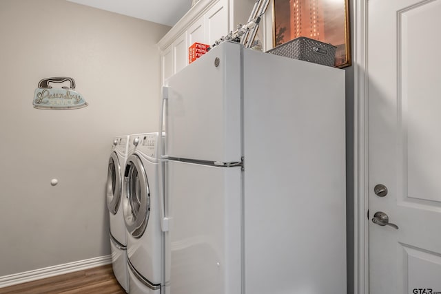 clothes washing area featuring dark wood-type flooring, washing machine and dryer, and cabinets