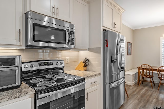 kitchen with appliances with stainless steel finishes, tasteful backsplash, ornamental molding, light stone countertops, and light wood-type flooring