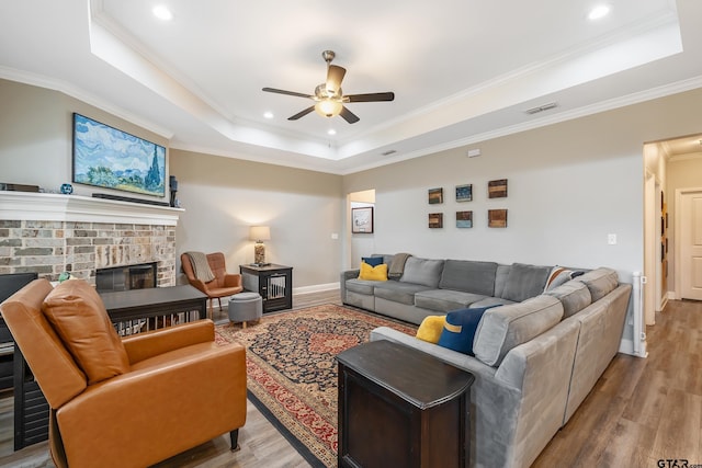 living room featuring a fireplace, ceiling fan, a raised ceiling, crown molding, and light hardwood / wood-style flooring