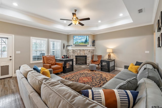 living room featuring crown molding, a tray ceiling, a fireplace, and hardwood / wood-style flooring