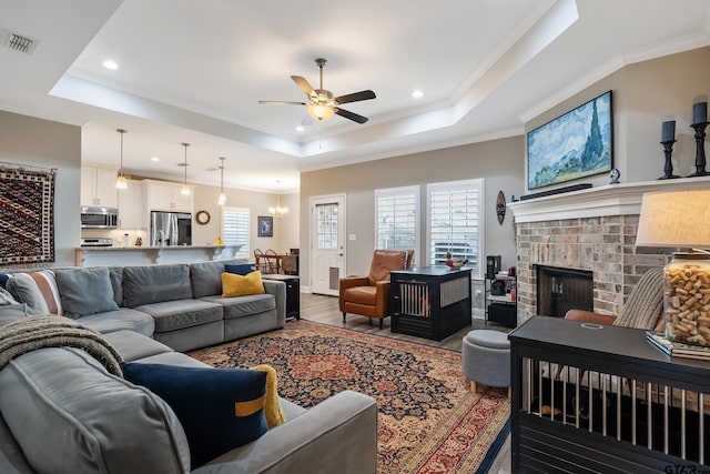 living room featuring hardwood / wood-style floors, a fireplace, ornamental molding, ceiling fan, and a tray ceiling