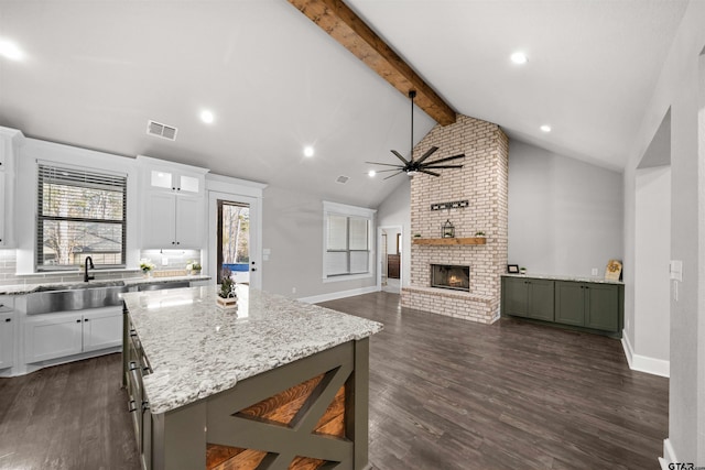 kitchen with white cabinetry, a brick fireplace, dark hardwood / wood-style flooring, a breakfast bar area, and a kitchen island