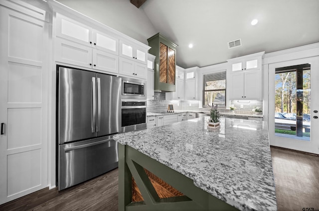 kitchen with white cabinets, decorative backsplash, vaulted ceiling with beams, light stone counters, and stainless steel appliances