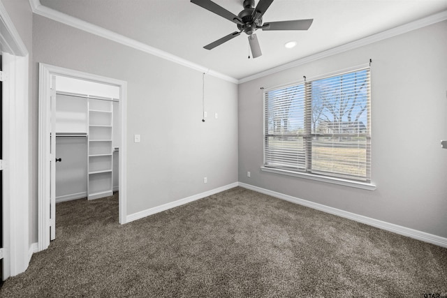 unfurnished bedroom with a walk in closet, dark carpet, ceiling fan, crown molding, and a closet