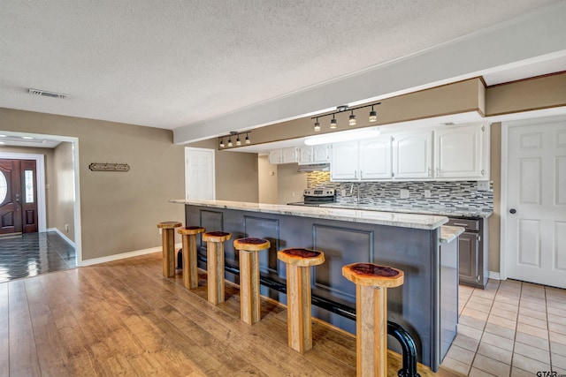 kitchen with rail lighting, light hardwood / wood-style flooring, tasteful backsplash, white cabinetry, and a breakfast bar area