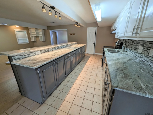 kitchen with a center island, sink, decorative backsplash, light stone counters, and white cabinetry