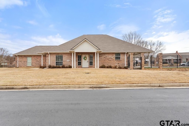 view of front of house with a shingled roof, a front yard, brick siding, and fence