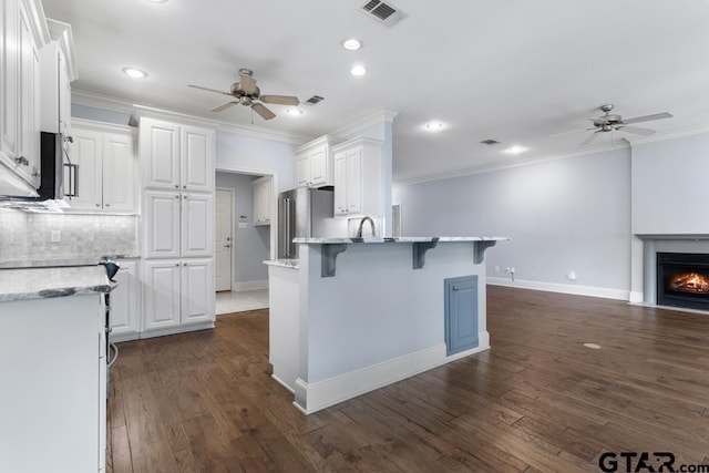 kitchen with freestanding refrigerator, a breakfast bar, visible vents, and white cabinetry