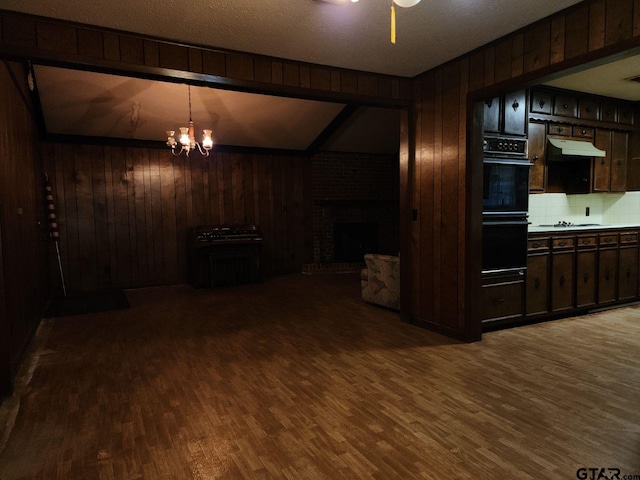 kitchen with dark brown cabinetry, hardwood / wood-style flooring, a brick fireplace, wooden walls, and vaulted ceiling