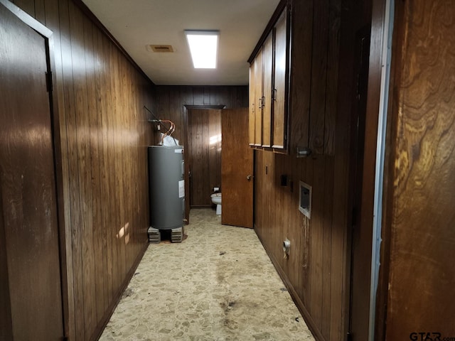 hallway featuring light carpet, wooden walls, and electric water heater