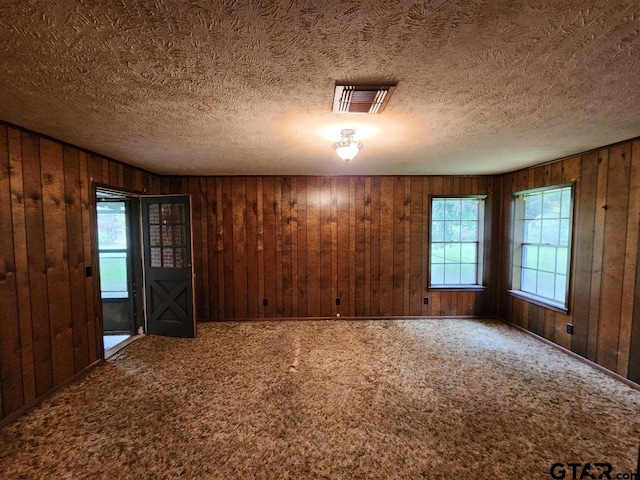 carpeted empty room featuring wooden walls and a textured ceiling