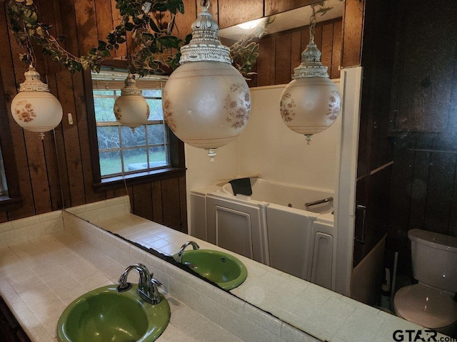 bathroom featuring toilet, wood walls, vanity, and a bathing tub