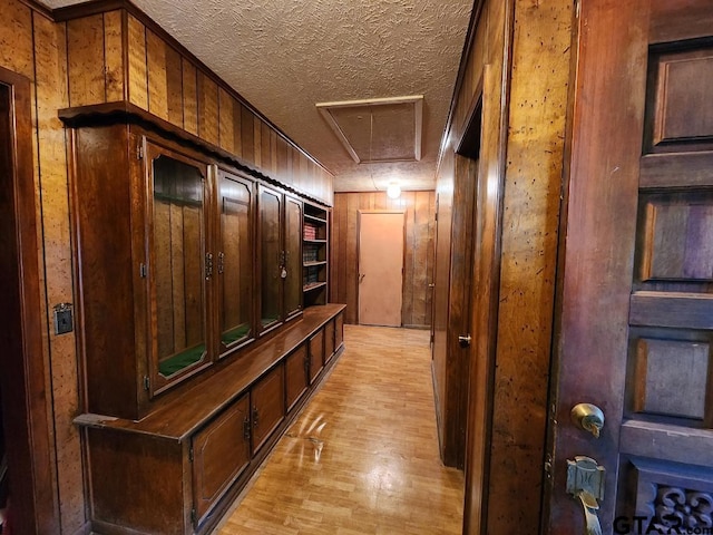 hall with a textured ceiling, light hardwood / wood-style floors, and wooden walls