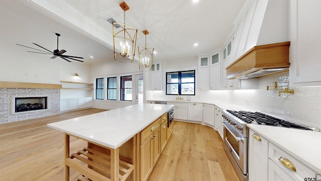 kitchen featuring white cabinetry, light hardwood / wood-style floors, stainless steel stove, and hanging light fixtures