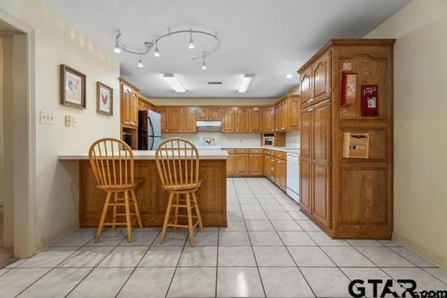 kitchen with dishwasher, kitchen peninsula, stainless steel fridge, a kitchen bar, and light tile patterned floors