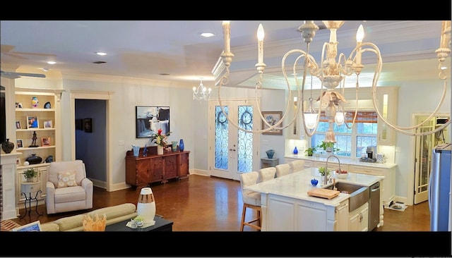 kitchen featuring ornamental molding, a notable chandelier, sink, white cabinets, and a kitchen island with sink