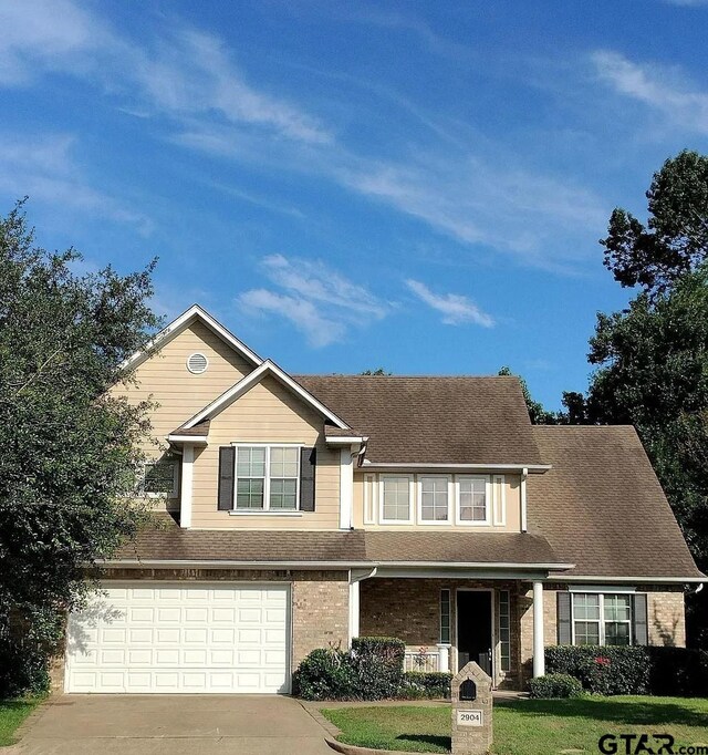 view of front of home with driveway, a front yard, a porch, a garage, and a shingled roof