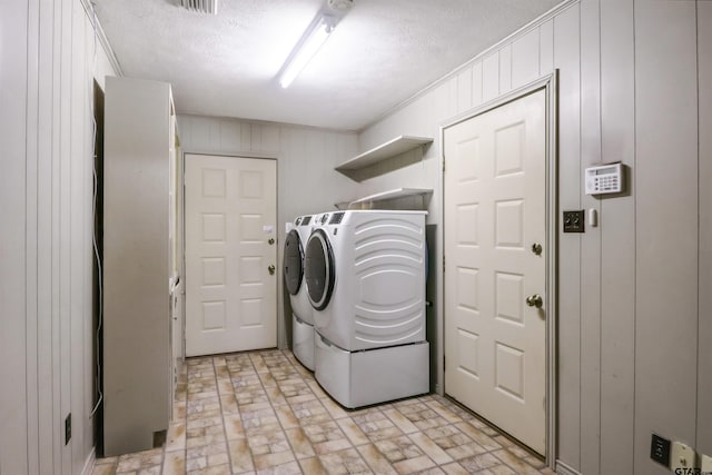 washroom featuring a textured ceiling, wooden walls, and independent washer and dryer