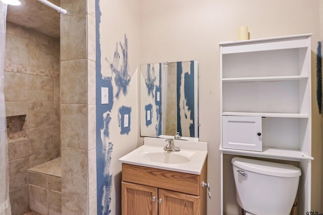 bathroom with a tile shower, vanity, and toilet