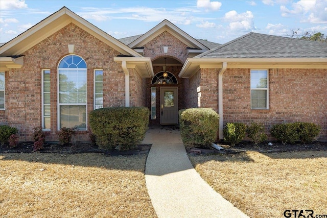 view of exterior entry featuring brick siding and roof with shingles