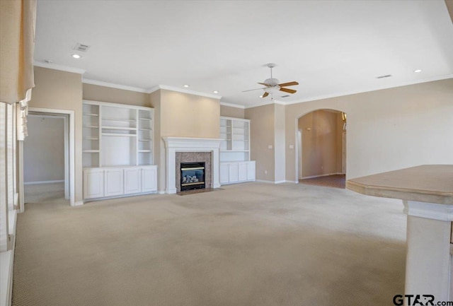 unfurnished living room with arched walkways, a fireplace, crown molding, light colored carpet, and a ceiling fan