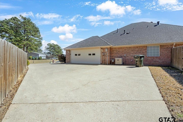 view of side of home featuring driveway, brick siding, an attached garage, and fence