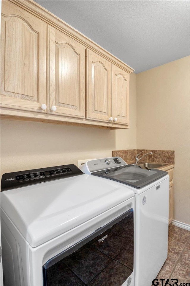 clothes washing area with cabinet space, baseboards, a textured ceiling, separate washer and dryer, and a sink