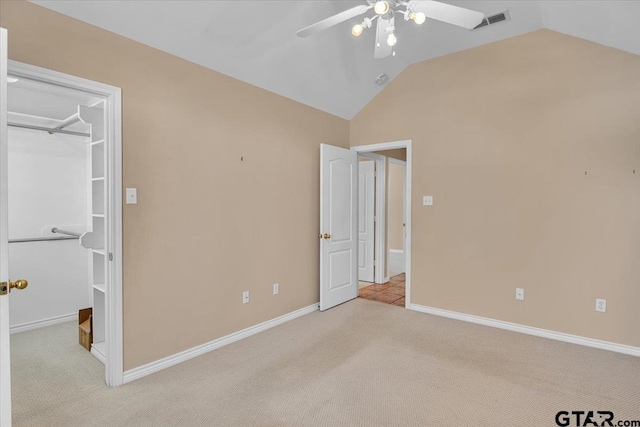 unfurnished bedroom featuring visible vents, light colored carpet, vaulted ceiling, and a spacious closet