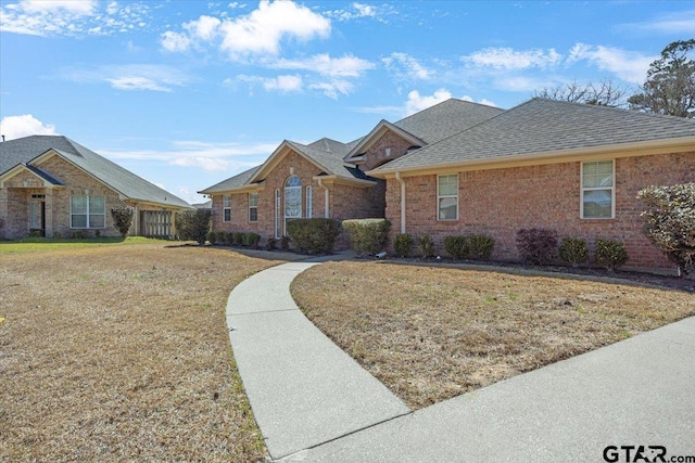 ranch-style home featuring brick siding, a front lawn, and roof with shingles