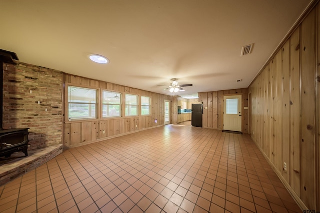2929 Dinah Ln, Tyler, TX 75701 - unfurnished living room with ceiling fan, a wood stove, wood walls, and tile patterned flooring