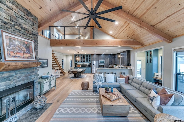 living room with beam ceiling, stairway, a stone fireplace, and light wood-style floors