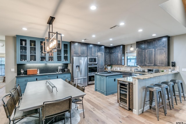 kitchen featuring a breakfast bar area, beverage cooler, visible vents, stainless steel appliances, and glass insert cabinets