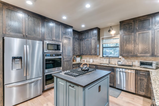 kitchen featuring a sink, stainless steel appliances, light wood-style floors, and decorative backsplash