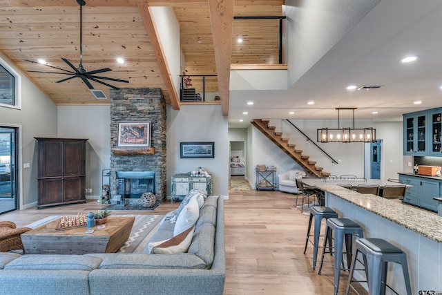 living room featuring stairway, a fireplace, recessed lighting, light wood-style floors, and ceiling fan with notable chandelier