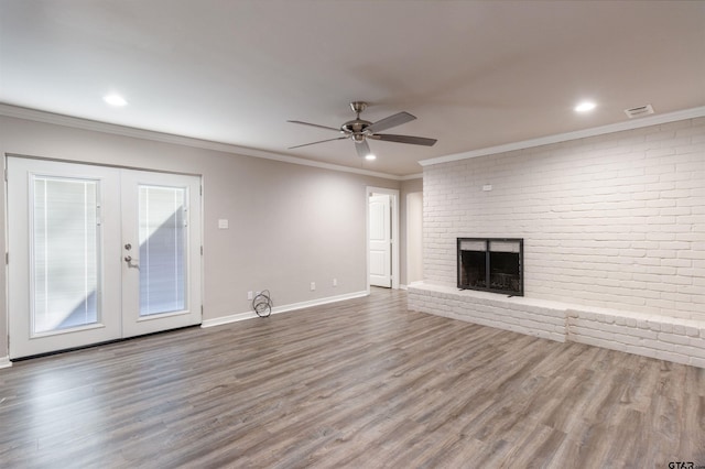 unfurnished living room featuring wood finished floors, french doors, brick wall, a fireplace, and crown molding