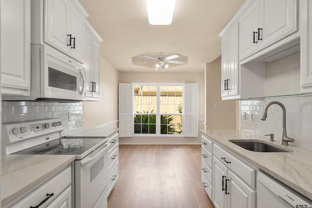 kitchen with white appliances, white cabinets, sink, backsplash, and light stone counters