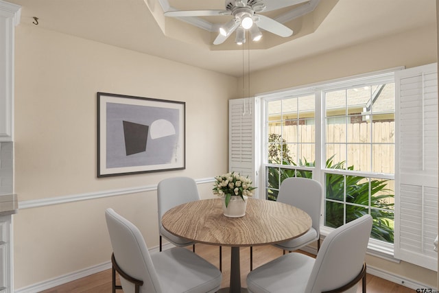 dining area with hardwood / wood-style floors, ceiling fan, and a raised ceiling