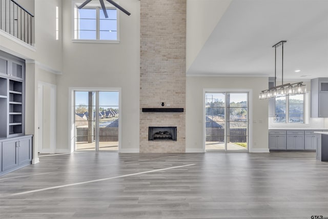 unfurnished living room with a large fireplace, ornamental molding, a high ceiling, and light hardwood / wood-style flooring